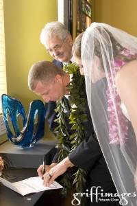 Groom signing the marriage certificate while bride and minister watch.